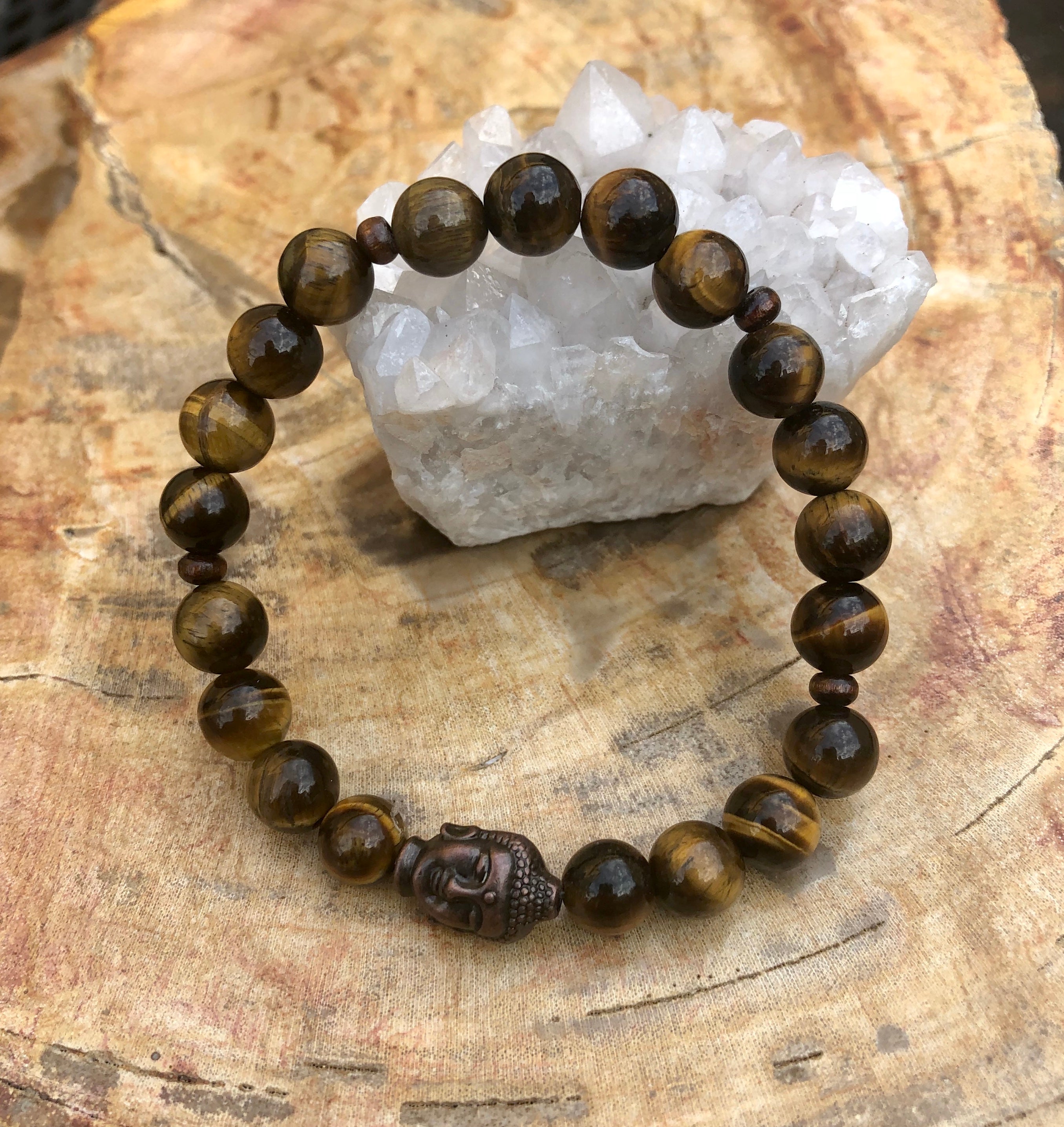 Beaded bracelet with Buddha head charm on a wooden surface with crystal rock