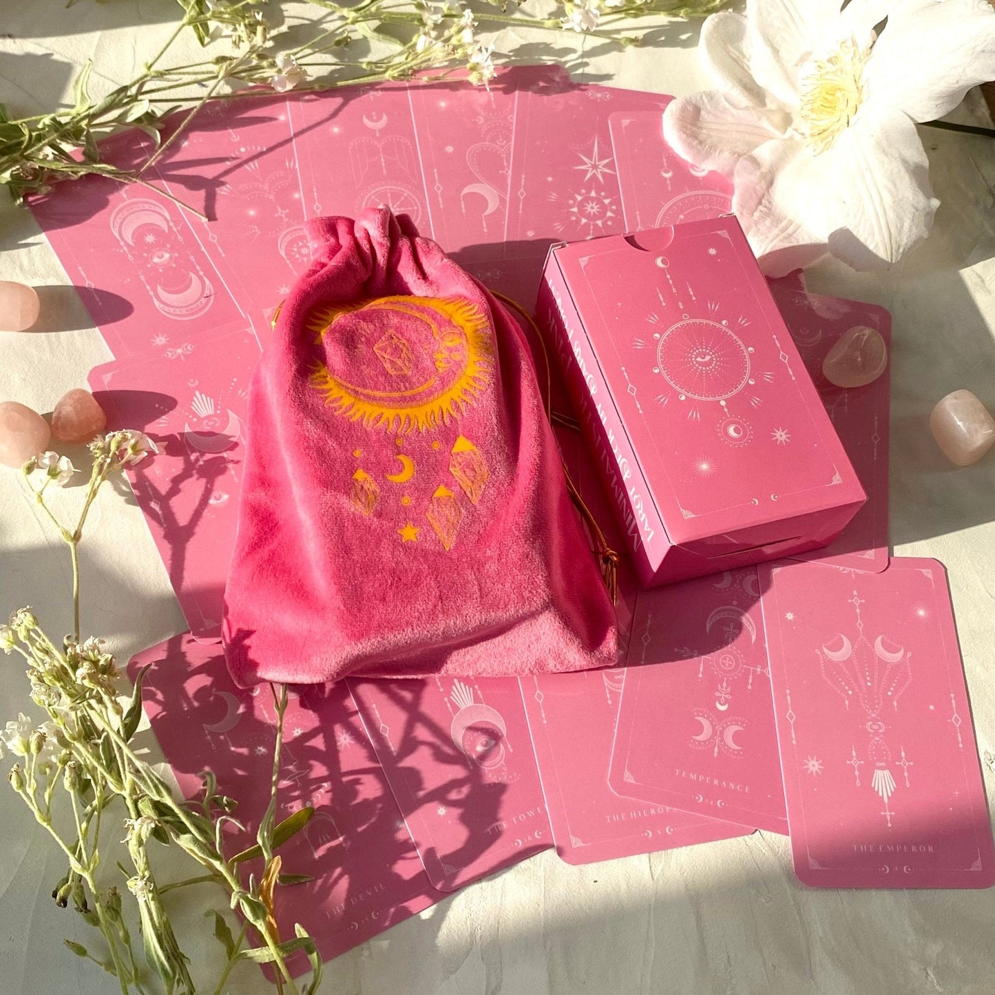 Pink tarot card set with a drawstring bag on a light surface with flowers.